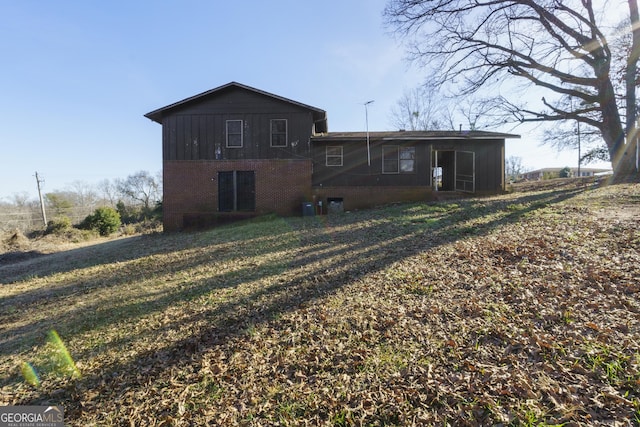 rear view of house with central AC unit and a lawn