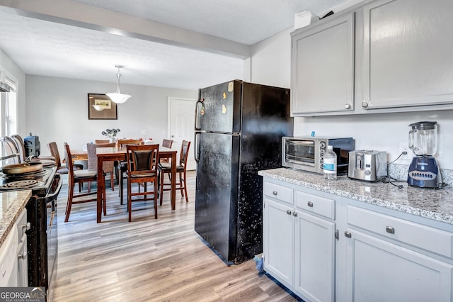 kitchen featuring light hardwood / wood-style flooring, hanging light fixtures, light stone counters, black appliances, and a textured ceiling