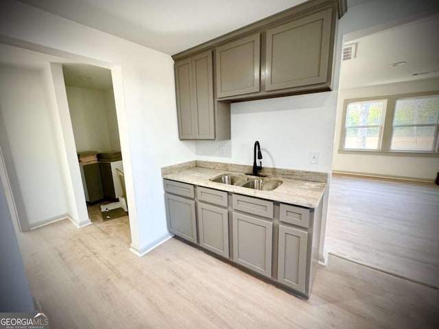 kitchen featuring gray cabinets, light stone countertops, sink, and light hardwood / wood-style floors