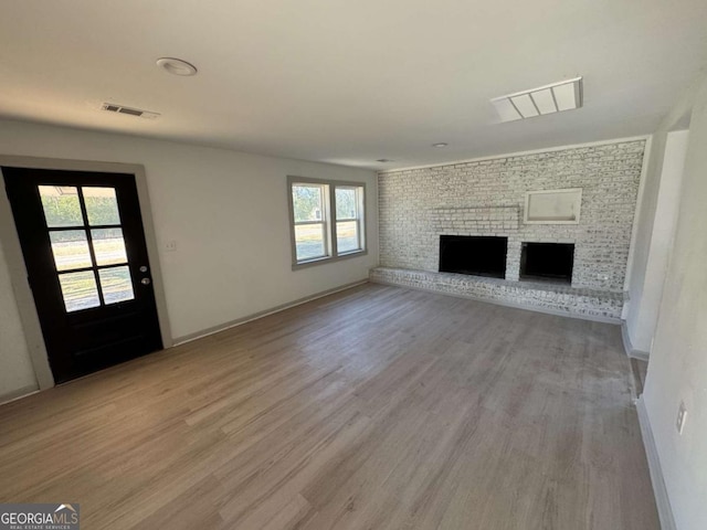 unfurnished living room with a brick fireplace and light wood-type flooring