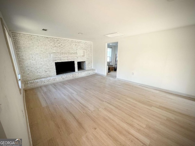 unfurnished living room with brick wall, a fireplace, and light wood-type flooring