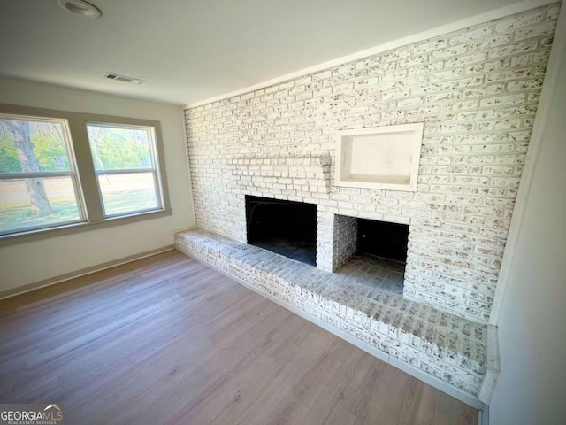 unfurnished living room featuring hardwood / wood-style flooring and a brick fireplace