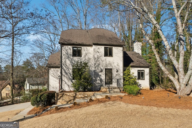 view of front of home with a shingled roof, a chimney, and stucco siding