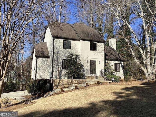 view of front facade featuring roof with shingles, a chimney, and stucco siding