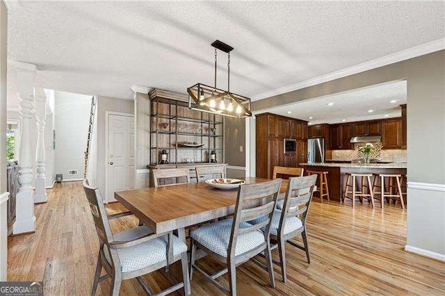 dining space with light wood-style floors, ornamental molding, and a textured ceiling