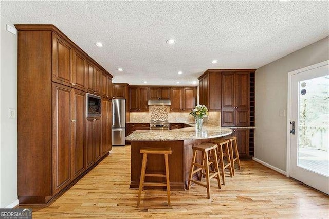 kitchen with stainless steel appliances, light wood-style flooring, under cabinet range hood, and a breakfast bar area