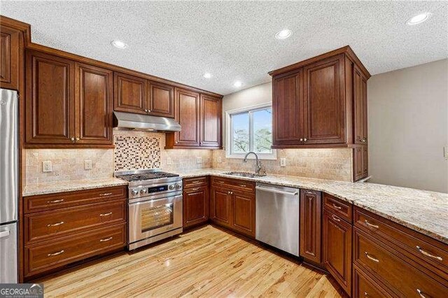 kitchen featuring under cabinet range hood, a sink, light wood-style floors, appliances with stainless steel finishes, and light stone countertops