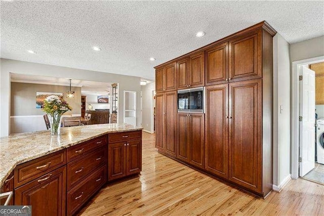 kitchen with a textured ceiling, light wood-style floors, light stone counters, and built in microwave