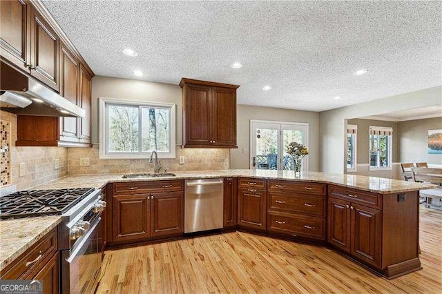 kitchen featuring light wood-style flooring, appliances with stainless steel finishes, light stone counters, a peninsula, and a sink