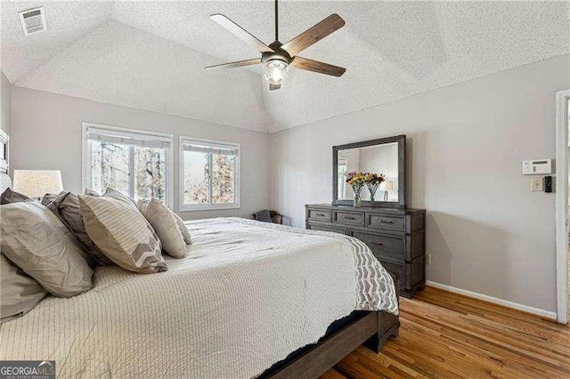 bedroom featuring visible vents, vaulted ceiling, a textured ceiling, wood finished floors, and baseboards