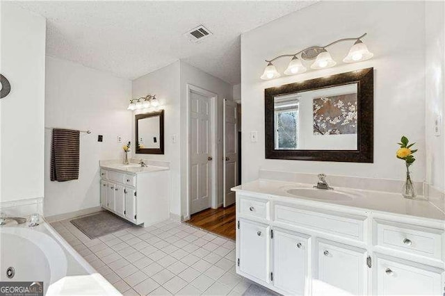 full bathroom featuring a textured ceiling, tile patterned flooring, a sink, visible vents, and a bath