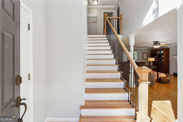 staircase featuring crown molding, wood finished floors, decorative columns, and a ceiling fan