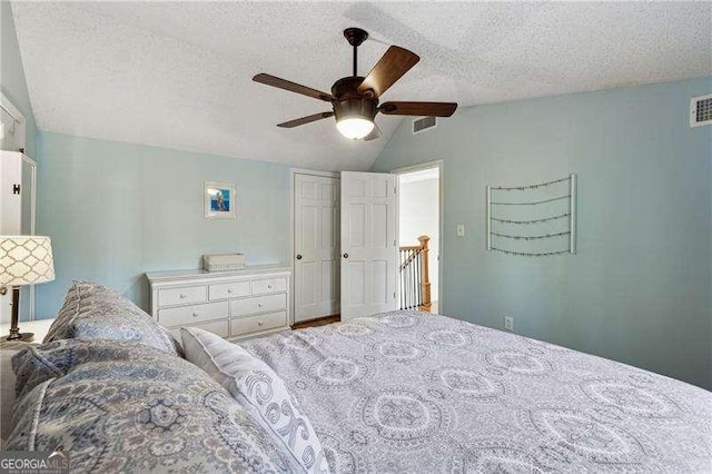 bedroom with lofted ceiling, visible vents, ceiling fan, and a textured ceiling