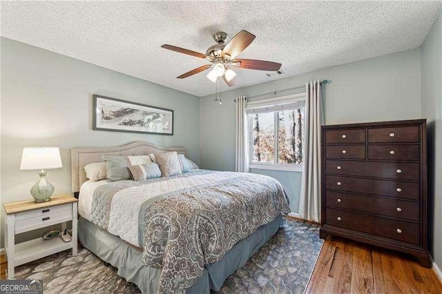 bedroom featuring a ceiling fan, visible vents, a textured ceiling, and wood finished floors