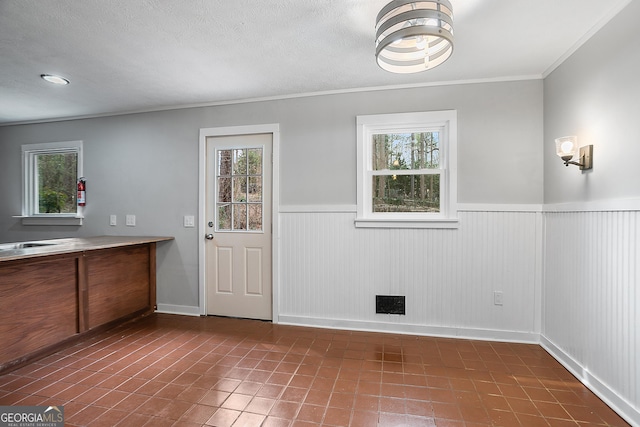 unfurnished dining area with wainscoting, plenty of natural light, visible vents, and crown molding