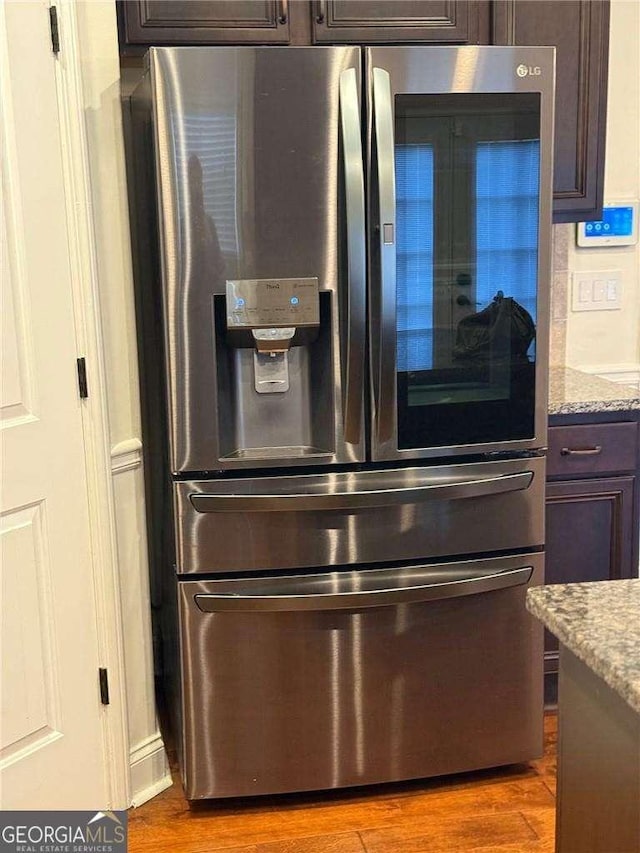 details featuring hardwood / wood-style flooring, dark brown cabinetry, light stone countertops, and stainless steel fridge with ice dispenser