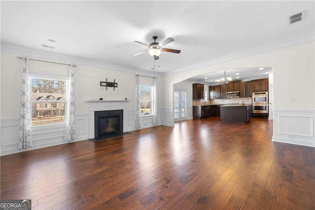 unfurnished living room featuring dark wood-type flooring, ornamental molding, and ceiling fan with notable chandelier