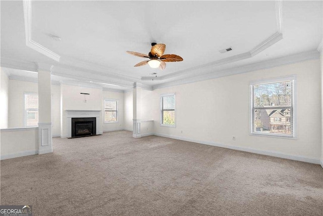 unfurnished living room featuring light colored carpet, ornamental molding, a tray ceiling, and ornate columns