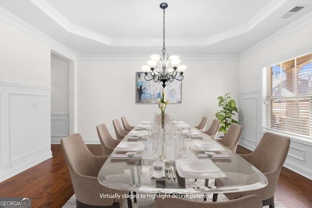 dining space with dark wood-type flooring, ornamental molding, a tray ceiling, and a notable chandelier