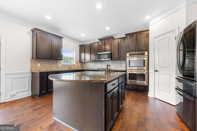 kitchen featuring stainless steel appliances, dark stone countertops, a center island with sink, and dark brown cabinetry