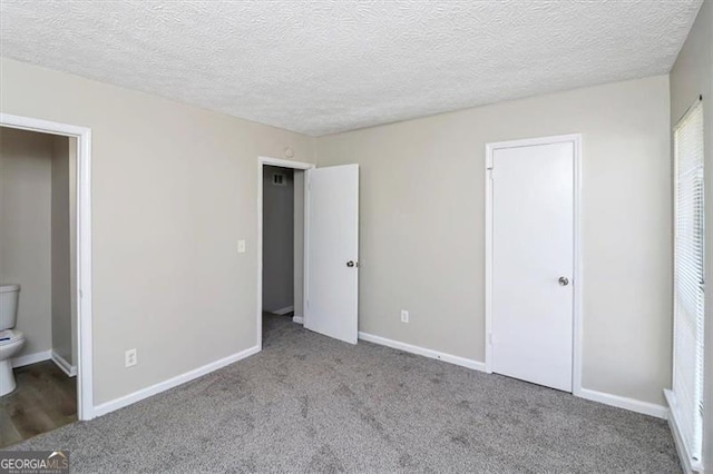 unfurnished bedroom featuring light carpet, a textured ceiling, and ensuite bathroom