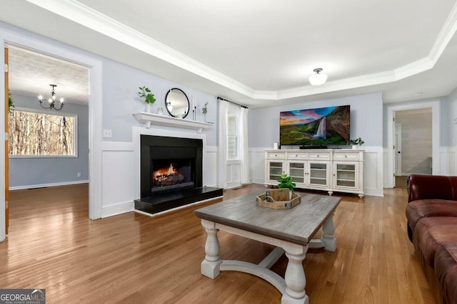 living room with crown molding, a chandelier, a raised ceiling, and hardwood / wood-style floors