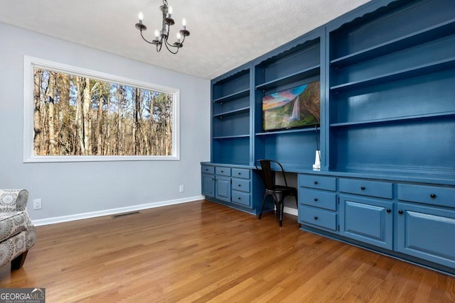 office area featuring hardwood / wood-style flooring, an inviting chandelier, built in desk, a textured ceiling, and built in shelves