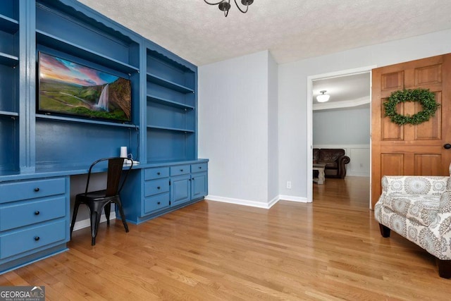 home office featuring built in shelves, built in desk, a textured ceiling, and light wood-type flooring