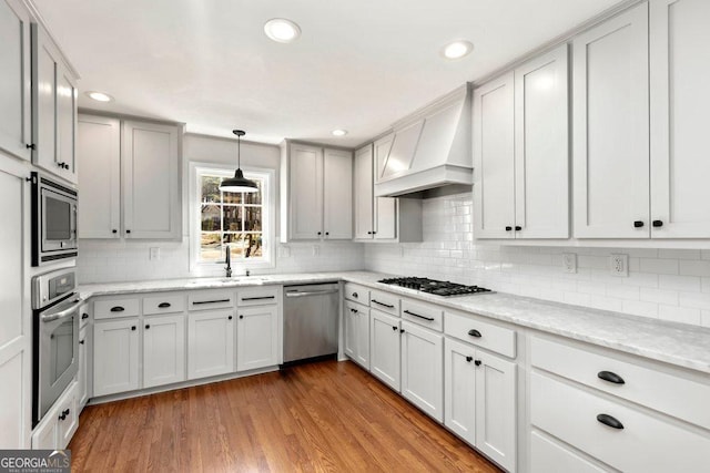 kitchen featuring sink, light hardwood / wood-style floors, stainless steel appliances, light stone countertops, and custom range hood