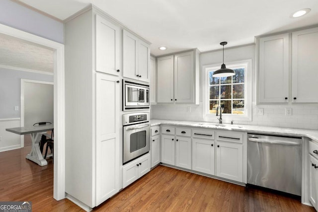 kitchen featuring sink, white cabinetry, hanging light fixtures, light wood-type flooring, and appliances with stainless steel finishes