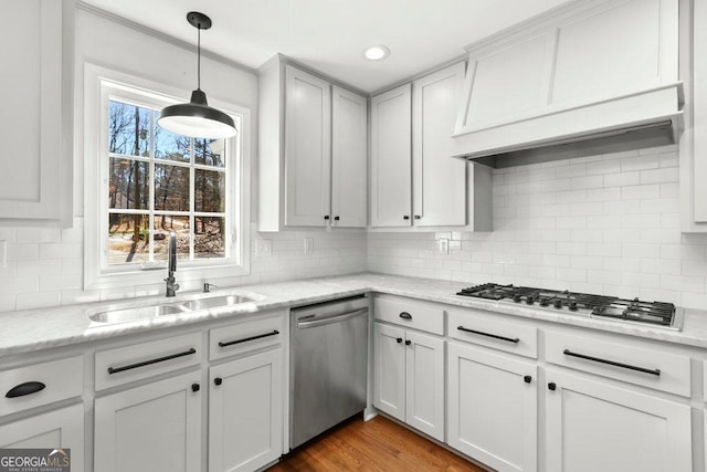 kitchen featuring premium range hood, white cabinetry, sink, light stone counters, and stainless steel appliances