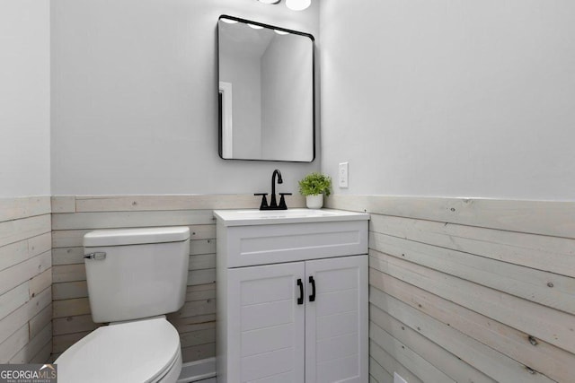 bathroom featuring vanity, wood walls, and toilet