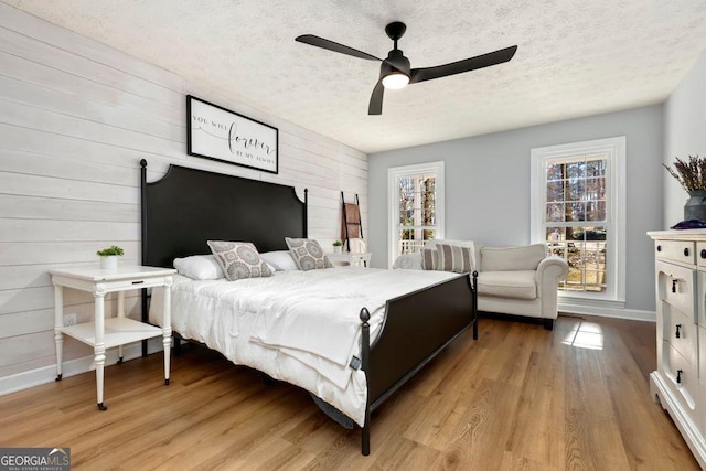 bedroom with ceiling fan, light hardwood / wood-style floors, a textured ceiling, and wood walls