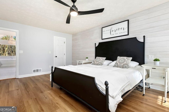 bedroom with ceiling fan, hardwood / wood-style floors, and wooden walls