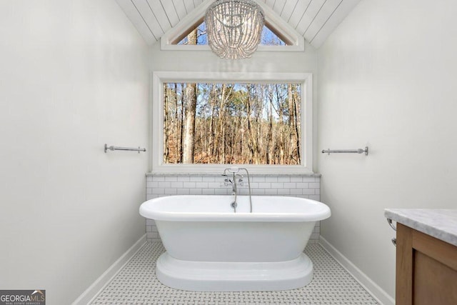 bathroom featuring an inviting chandelier, a tub to relax in, vaulted ceiling, and vanity