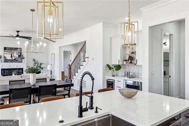 kitchen with pendant lighting, ornamental molding, white cabinets, decorative backsplash, and beverage cooler