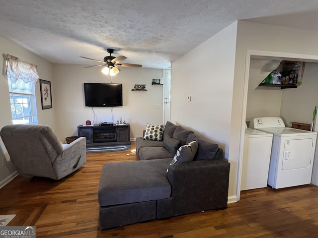 living room featuring ceiling fan, dark wood-type flooring, washing machine and clothes dryer, and a textured ceiling