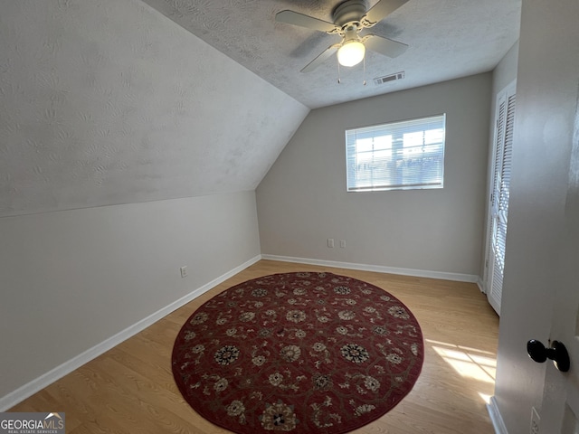 additional living space featuring vaulted ceiling, ceiling fan, a textured ceiling, and light hardwood / wood-style flooring