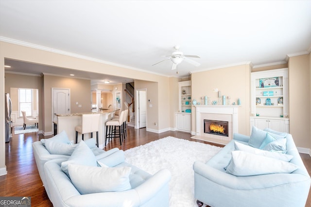 living room with dark wood-type flooring, ceiling fan, ornamental molding, and built in shelves