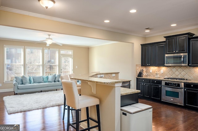 kitchen featuring appliances with stainless steel finishes, dark hardwood / wood-style floors, a kitchen breakfast bar, an island with sink, and backsplash