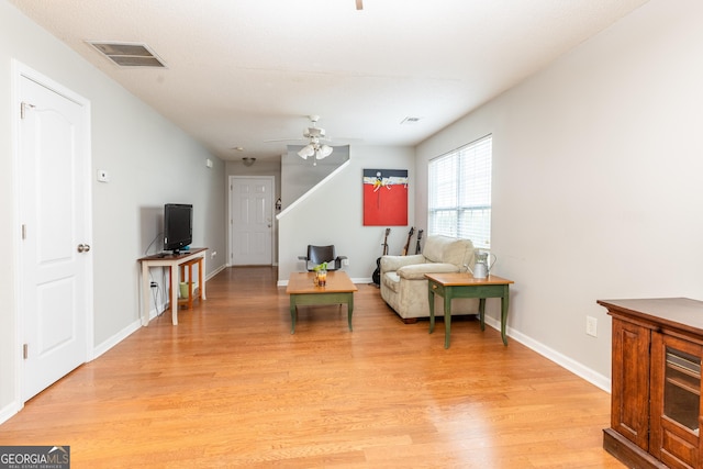 living room featuring baseboards, a ceiling fan, visible vents, and light wood-type flooring