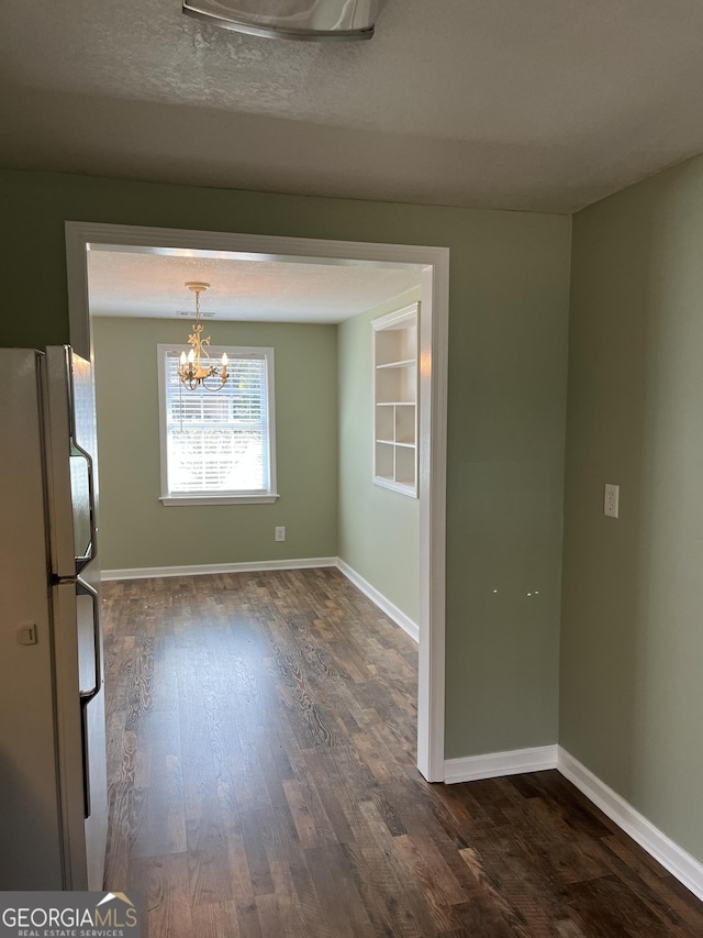 unfurnished dining area featuring dark wood-type flooring, a notable chandelier, and a textured ceiling