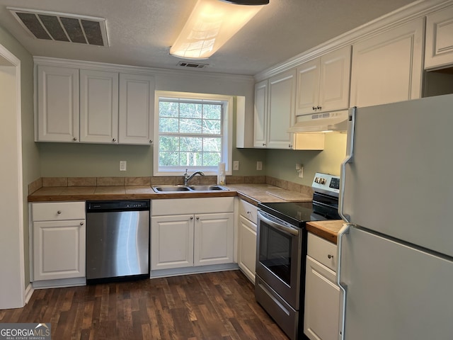 kitchen with appliances with stainless steel finishes, white cabinetry, sink, tile counters, and dark wood-type flooring