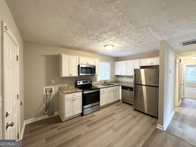 kitchen with a healthy amount of sunlight, light hardwood / wood-style flooring, white cabinets, and appliances with stainless steel finishes