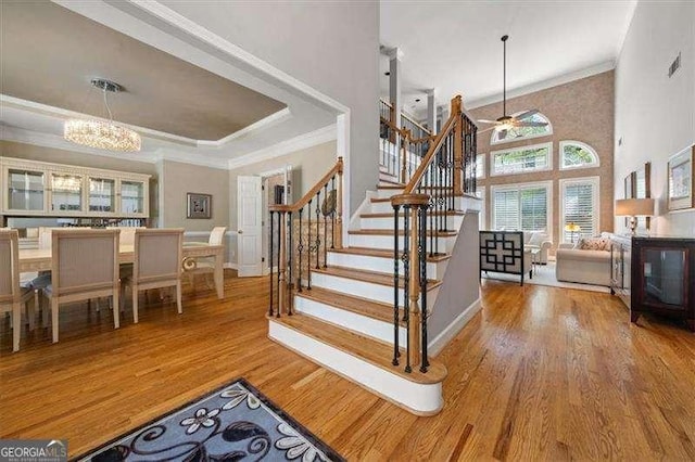 stairway with ceiling fan with notable chandelier, hardwood / wood-style floors, a high ceiling, ornamental molding, and a tray ceiling