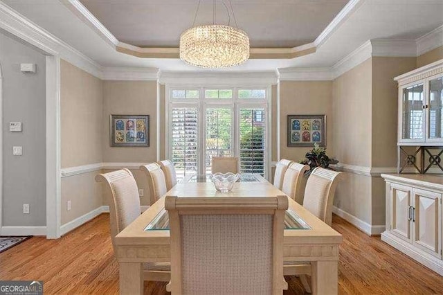 dining space featuring a raised ceiling, ornamental molding, a chandelier, and light hardwood / wood-style floors