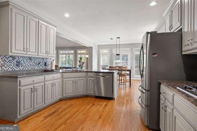 kitchen with tasteful backsplash, hanging light fixtures, light hardwood / wood-style flooring, appliances with stainless steel finishes, and kitchen peninsula