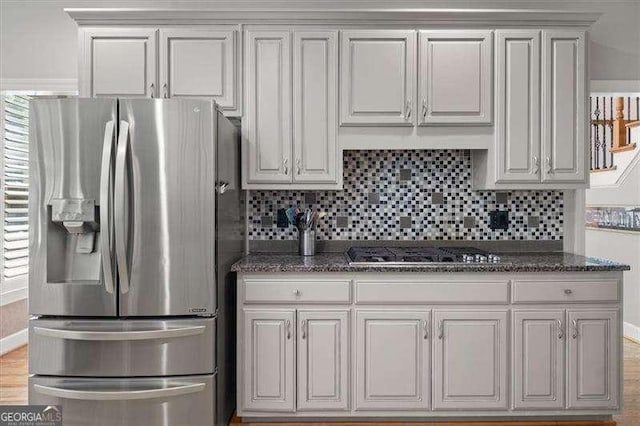 kitchen featuring black gas stovetop, white cabinetry, dark stone countertops, backsplash, and stainless steel refrigerator with ice dispenser