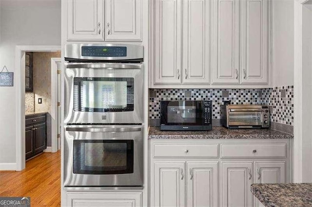 kitchen with tasteful backsplash, white cabinetry, light wood-type flooring, and double oven