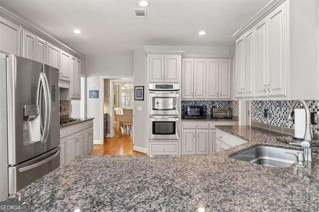 kitchen featuring sink, white cabinetry, stainless steel appliances, tasteful backsplash, and dark stone counters